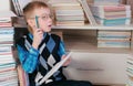 Seven-year-old boy with glasses thinking and draws something in a sketchbook sitting among the books. Royalty Free Stock Photo