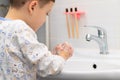 A seven-year-old boy in pajamas is washing his hands at home in a bright bathroom over a washbasin against the backdrop of tiles a Royalty Free Stock Photo