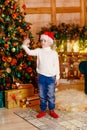 a boy in Santa`s cap with a phone in his hands stands near a large elegant Christmas tree. A child takes a selfie