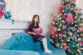 A seven-year-old girl with black hair in a purple dress holds a gift box in her hands near a Christmas tree indoors. pink feathers Royalty Free Stock Photo