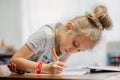 A seven-year-old girl sits at home at a table and writes in a notebook, completing a learning task or repeating lessons. Royalty Free Stock Photo