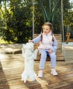 A seven-year-old girl swings on a swing and plays with a dog in a summer park Royalty Free Stock Photo