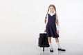 A seven year old school girl in a school uniform poses on a white or light background