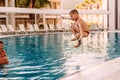 Seven-year-old tanned boy jumping, legs tucked in the outdoor pool at the resort Royalty Free Stock Photo