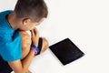 Seven years old boy sits down on the floor close to tablet computer with broken screen glass.