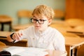 Seven years old child with glasses writing his homework at school. Boy studing at table on class background