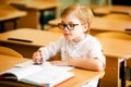 Seven years old child with glasses writing his homework at school. Boy studing at table on class background