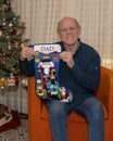 Seventy-three year-old Caucasian man posing by his Christmas tree with his handmade `Dad` Christmas stocking in Dallas, Texas.