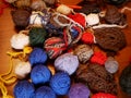 Several balls of multicolored woolen threads lie on a wooden table. The yarn is prepared for needlework.