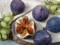 Several berries of figs and small bunches of grapes lie on a table on a circle of natural sawn wood and a linen napkin.