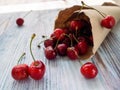 Several berries of ripe cherries on a wooden table in drops of water. The rest of the berries are in a paper bag.