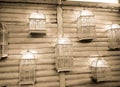 Several bird cages with lights hanging on a white log wall