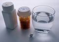 Several bottles with diverse medication next to a glass of water