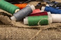 Several coils of multicolored sewing thread against a background of coarse-textured burlap. Close up