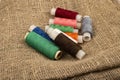 Several coils of multicolored sewing thread against a background of coarse-textured burlap. Close up