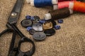 Several colored buttons of different sizes, reels of colored sewing thread, and large vintage sartorial scissors against a