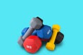 Several colored dumbbells stand in a pile, on a turquoise background, the concept of sport and lifestyle