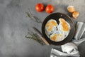 Several fried eggs with tomato and thyme in a pan on a gray background, knife, towel, shell, top view