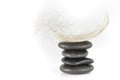 Several gray stones lie on top of one another on top of which lies a feather against a white background