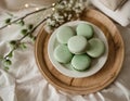 Several green, pastel macaroons placed on a plate, on a wooden tray lying on the bed linen