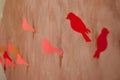 Several handmade red paper birds in line hanging on bast string on wall brouwn bacground. Red paper bird on the clothesline.