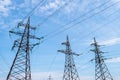 Several high voltage towers against a blue cloudy sky. Power lines. Horizontal photo, electricity concept. Royalty Free Stock Photo