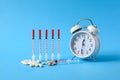 Several insulin syringes next to an alarm clock on a blue background.