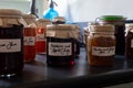 Several jars of home made jams sitting on a work top, with old fashioned brown paper and string lids with hand written