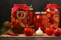 Several jars tomatoes are located on a table, on a dark background