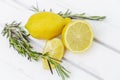 Several lemons,. whole and sliced, sitting on top a light wooden table. Close-up, top view. Rosemary leaves