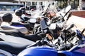 Several motorcycles and mopeds of all types parked in a row standing on a sidewalk in a European city