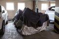 Several motorcycles stand in row covered with dust protective canvas covers for safekeeping during winter