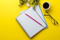 Several notebooks and glasses a cup of coffee and flowers on a bright yellow background. top view. office tools