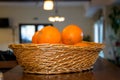 A wicker basket full of oranges, fresh citrus fruits on wooden table in a kitchen