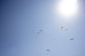 A several paragliders on colorful parachutes in a clear blue sky with a bright sun