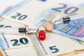 Several pills and syringes on euro banknotes, with coins.