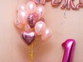 several pink helium balloons in the room, inflatable letters on the wall, and an inflatable number one below