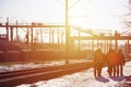 Several railway workers in signaling dirty orange uniforms are on the road next to the railway line. The train crew goes to work