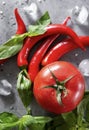 Several red chili peppers, green Basil sprigs, 1 red tomato, salt, spices, ice cubes on a gray