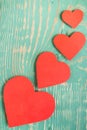 Several red paper hearts on light green painted textured with squiggly stripes wooden table.