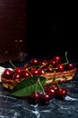 Several red sweet cherries and big green leaf on the table. Fresh organic cherry in yellow wooden basket on dark marble Royalty Free Stock Photo