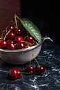 Several red sweet cherries and big green leaf on the table. Fresh organic cherry in colander on dark marble background.. Royalty Free Stock Photo