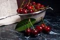 Several red sweet cherries and big green leaf on the table. Fresh organic cherry in colander on dark marble background.. Royalty Free Stock Photo