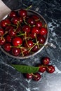 Several red sweet cherries and big green leaf on the table. Fresh organic cherry in colander on dark marble background.. Royalty Free Stock Photo