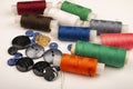 Several reels of multicolored sewing thread and multicolored buttons of different sizes on a white background. Close up Royalty Free Stock Photo