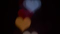 Several refocusing flashing colorful hearts on a black background. Blurry bokeh