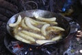 Several ripe bananas are fried in a deep frying pan in oil over a campfire.