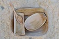 Several roughly carved wooden bowls and a spoon sittng on the sawdust covered ground