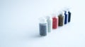 Several small cans with colored beads for manicure stand in a row on a white background.