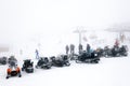 Several snowmobiles stand abreast on the top of the mountain in